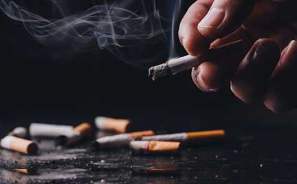 A hand holding a cigarette with more cigarettes in the background