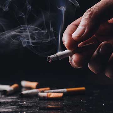 A hand holding a cigarette with more cigarettes in the background