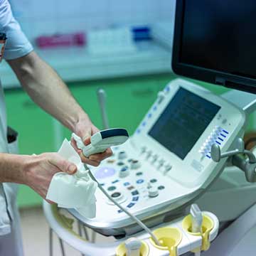 A person in scrubs cleaning a probe of an ultrasound examination
